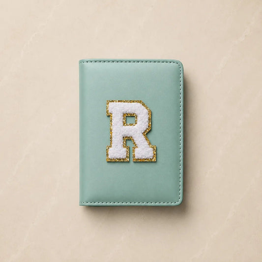 Personalized mint green vegan leather passport cover featuring a white chenille initial 'R' varsity letter patch with a gold glitter border.